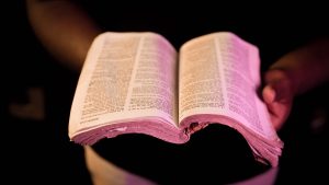 An open Bible held in hands with dramatic lighting, creating a serene atmosphere.